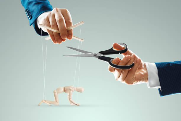 A man's hand cuts the threads between the puppeteer and the puppet with scissors. The concept of liberation from slavery, freedom, shadow government, world conspiracy, manipulation, control. stock photo