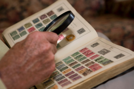 Teen girl with magnifier looks his stamp collection  isolated