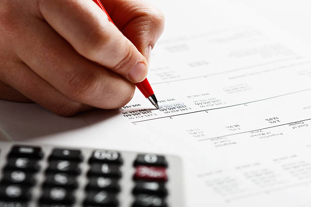 Man's hand marking items on financial document with calculator nearby A person's hand checks a financial document, marking items off with a ballpoint pen, a calculator  standing by. Could be home or office finances being checked so carefully.  iridium stock pictures, royalty-free photos & images