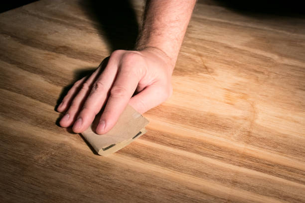 Man's hand sanding with grain of wood using sheet of fine sandpaper, to prepare for painting or refinishing. stock photo