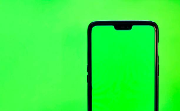 Man's hand shows mobile smartphone with green screen isolated on green background. Mock up mobile  smart phone green background stock pictures, royalty-free photos & images