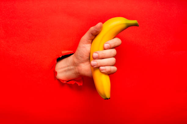 Man's hand with ripe yellow banana ripped from red-colored paper, advertisement sample with free space for logo. stock photo