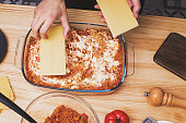 Man's hands making layers of lasagna in glass tray, top view. Cooking at home, traditional italian dish