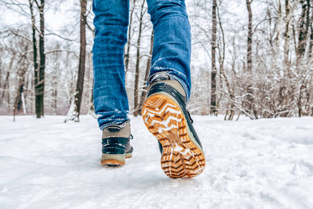 Man's legs in black with orange boots walking in the snow stock photo
