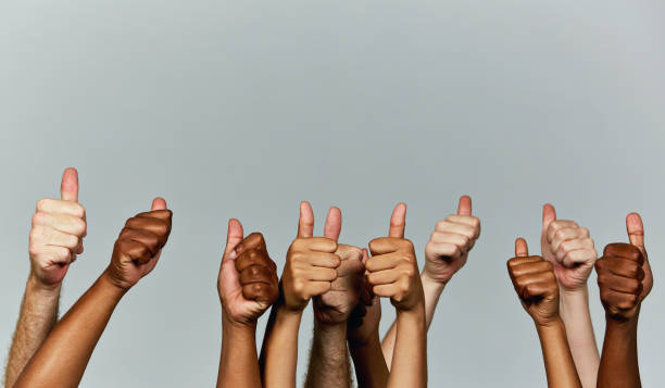 Many hands giving enthusiastic thumbs-up signals against gray background stock photo