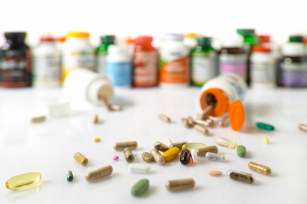 Many nutritional health supplements and vitamins in capsules, tablets and in bottles on a white background, shallow depth of focus. Colorful display and stack of many types of nutritional supplements and vitamin plastic bottles in an out of focus background with many supplement and vitamin capsules and pills in focus in the foreground. Scene set on a white background. vitamin stock pictures, royalty-free photos & images