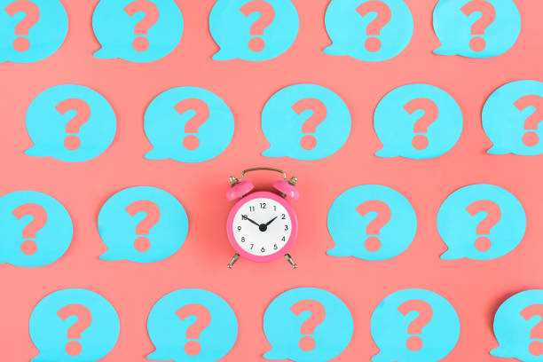 Many pink stickers with question marks are on the pink background. In the center is a small alarm clock. Concept, a matter of time. stock photo