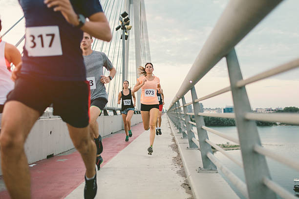 Marathon Runners. Runners running marathon in the city. They are running over the bridge at sunset. Wearing numbers on their sport clothes. Cityscape in background. marathon stock pictures, royalty-free photos & images