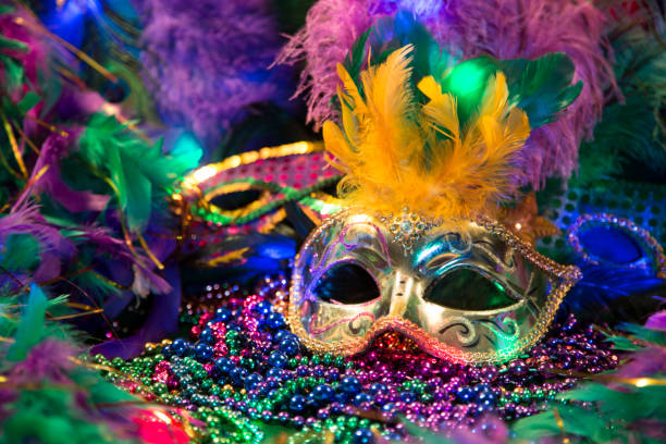 LV Mardi Gras sequined mask, decorated with feathers on a bed of feathered Mardi Gras feather Boas.  Colorful beads and spot lights of color. stock photo