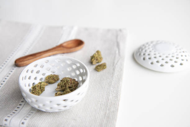 Marijuana Buds in a Porcelain Bowl on a Silver Placemat with Wooden Spoon and Lid - Minimalist Cannabis stock photo