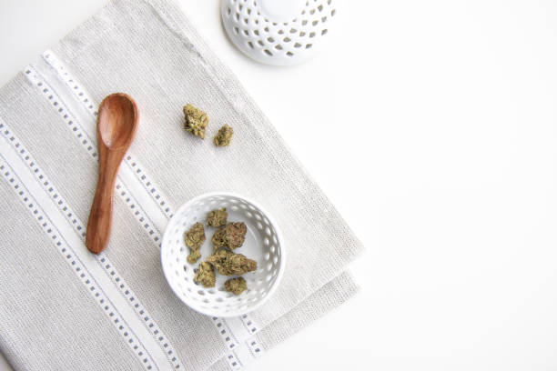 Marijuana Buds in a Porcelain Bowl on a Silver Placemat with Wooden Spoon and Lid Top Down View - Minimalist Cannabis stock photo