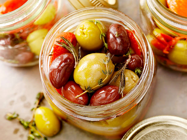 Marinated Olives Marinated Olives with Roasted Red Peppers, Garlic, Fresh Thyme and Rosemary in Glass Jars for Preserving-Photographed on Hasselblad H3D2-39mb Camera green olives jar stock pictures, royalty-free photos & images