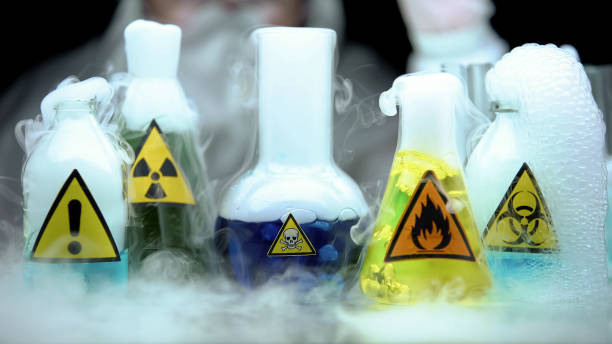 Marked dangerous liquids evaporating in flasks in front laboratory worker stock photo