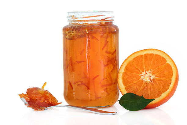 Marmalade Jam "Marmalade in a jar with half an orange, leaf and jam in a spoon over white background." marmalade stock pictures, royalty-free photos & images