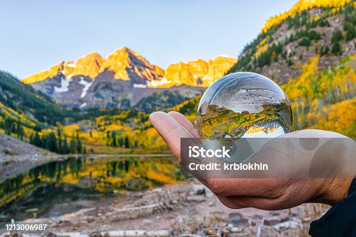 istock Maroon Bells lake at sunrise with hand holding crystal ball reflection in Aspen, Colorado with rocky mountain peak and snow in October 2019 autumn and vibrant trees 1213006987