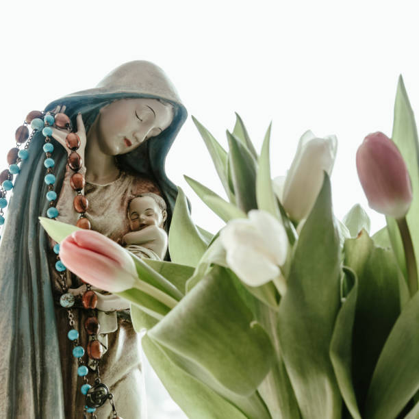 Mary with Jesus statue with tulips, backlit stock photo