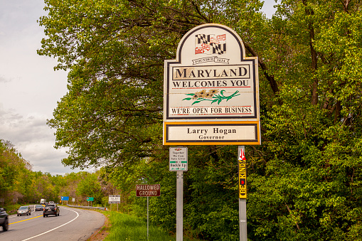 Point of Rocks, MD, USA 04-30-2021: Maryland Welcomes You road sign on the scenic byway US Route 15 at the border of Maryland and Virginia.  It has MD flag and says open for business.