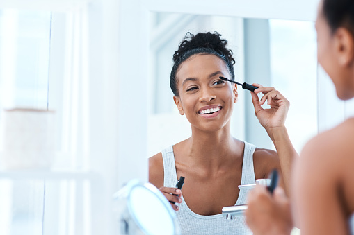 Shot of a beautiful young woman applying mascara in her bathroom mirror