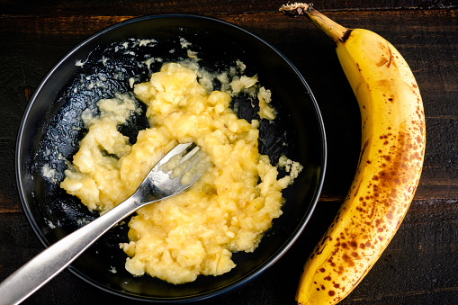 A bowl of mashed banana with a whole banana next to it