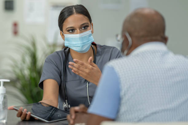 Masked Medical Appointment A senior patient and a female doctor meet in a medical clinic while wearing protective face masks to avoid the transfer of germs. patient stock pictures, royalty-free photos & images