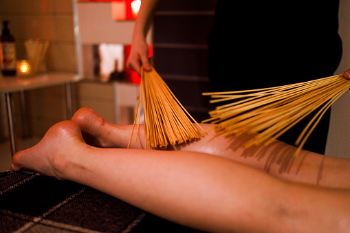 Masseur using bamboo massage broom on legs of female client
