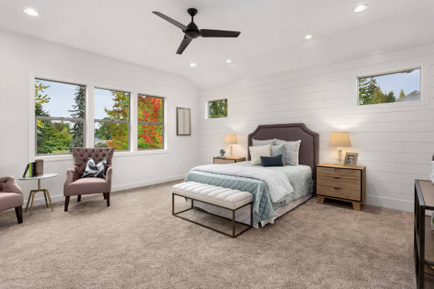 master bedroom in new luxury home with large windows, ceiling fan, carpet, and elegant decor. Master bedroom in luxury home carpet decor stock pictures, royalty-free photos & images