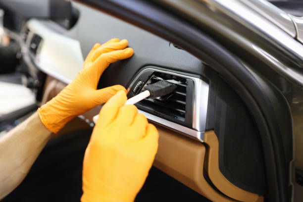Master repairman in rubber gloves cleaning car air conditioner with brush in workshop closeup stock photo