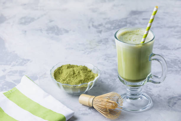 Matcha green tea latte. A healthy drink in a transparent glass, green tea powder and a bamboo whisk. Photo with place for text, copy space. stock photo