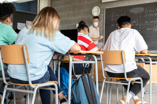 Mathematics class. Mature white male teacher wearing face mask in classroom with group of multiracial teen high school students. Mathematics class. Mature white male teacher wearing face mask in classroom with group of multiracial teen high school students. Education concept. Healthcare concept. coaching stock pictures, royalty-free photos & images