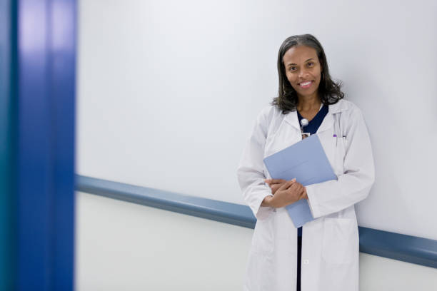 mature adult intern smiles as she stands in hospital corridor - doctor wall imagens e fotografias de stock