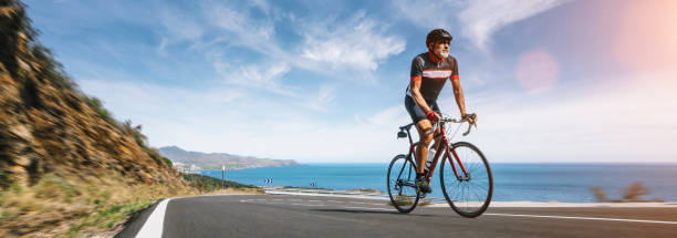 Mature Adult on a racing bike climbing the hill at mediterranean sea landscape coastal road stock photo