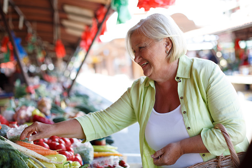 Happy senior lady is buying vegetables on farmer's market. All products are fresh and organic. It is important for health and well-being to consume groceries as fresh as possible.