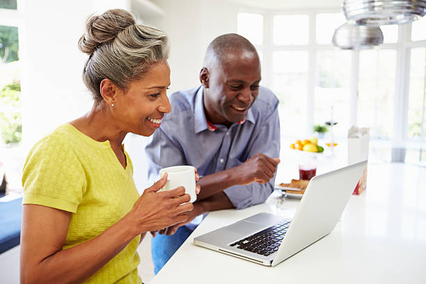 Mature African American couple using a laptop in a kitchen Mature African American Couple Using Laptop At Breakfast mature couple stock pictures, royalty-free photos & images