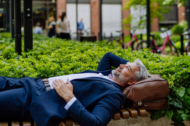 Mature businessman relaxing on bench in city park during break at work, work-life balance concept. stock photo
