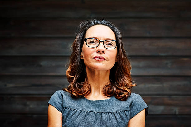 Mature businesswoman standing against a wooden wall in office Portrait of mature businesswoman standing against a wooden wall in office staring stock pictures, royalty-free photos & images