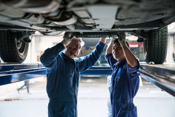 Mature car mechanic and apprentice at work Mature auto mechanic and apprentice checking vehicle chassis in the auto repair shop. auto mechanic stock pictures, royalty-free photos & images