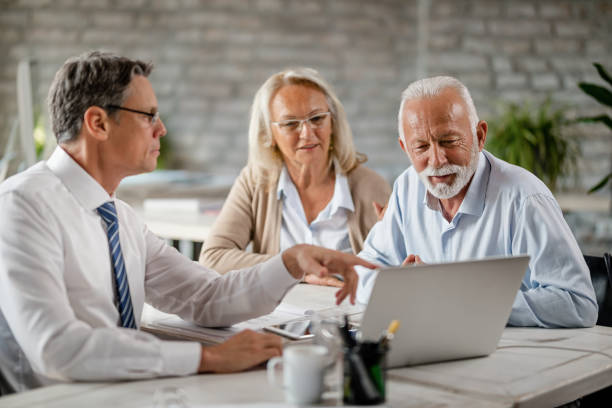 Mature couple and insurance agent using computer during consultations in the office. Senior couple using laptop with their financial advisor during a meeting int he office. Focus is on senior man. retirement stock pictures, royalty-free photos & images