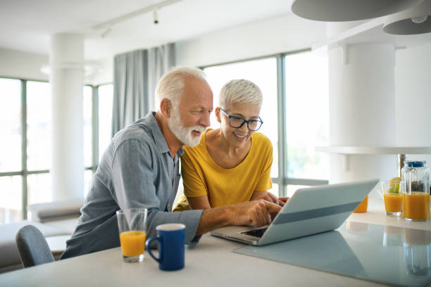 Mature couple buying some goods online Closeup top view of a mid 60's couple sitting at a kitchen counter and doing some online shopping. laptop couple stock pictures, royalty-free photos & images