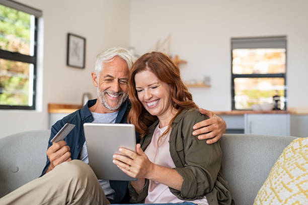 Mature couple doing online shopping with digital tablet Happy mature couple sitting on sofa and doing online shopping on digital tablet at home. Senior husband and smiling wife paying bills online. Joyful middle aged couple doing online payment on digital tablet, copy space. credit card purchase photos stock pictures, royalty-free photos & images