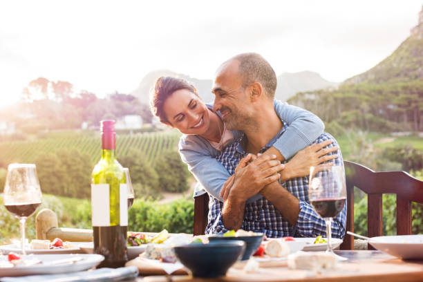 Mature couple in love Happy mature couple looking at each other while hugging after lunch. Smiling couple in love sitting at dining table. Happy woman embracing from behind her boyfriend outdoor. mid adult couple stock pictures, royalty-free photos & images