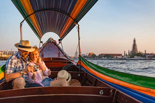 Mature couple in a traditional Asian longtail boat having a romantic sunset cruise on the Chao Phraya River in Bangkok, Thailand