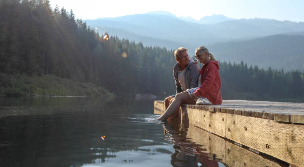 Mature couple relax on wooden pier, looks out across lake Lost Lake, Whistler, BC mature couple stock pictures, royalty-free photos & images