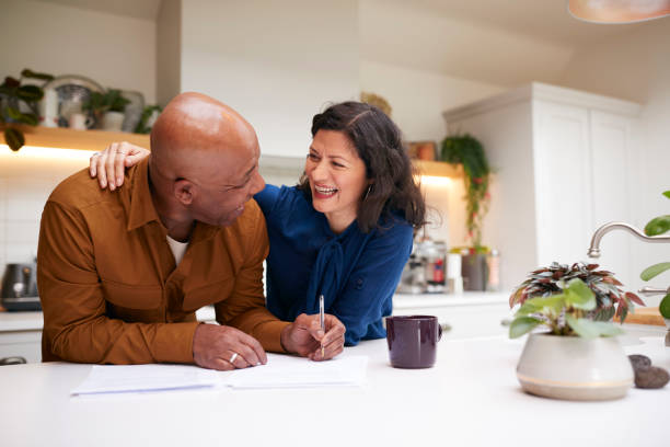 mature couple reviewing and signing domestic finances and investment paperwork in kitchen at home - reforma assunto imagens e fotografias de stock
