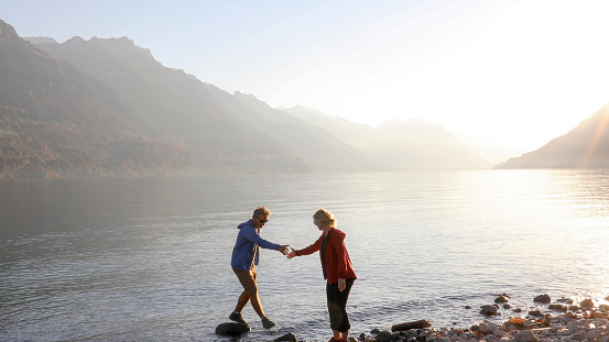 Woman offers man a helping hand, Swiss Alps visible across the water