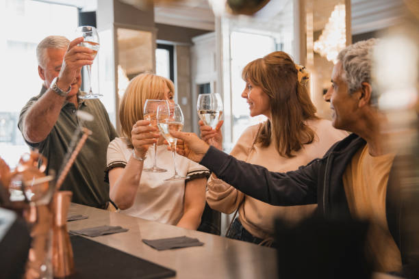 Mature Couples Toasting at the Bar Two mature couples are making a toast at a bar with white wine. 50 59 years stock pictures, royalty-free photos & images