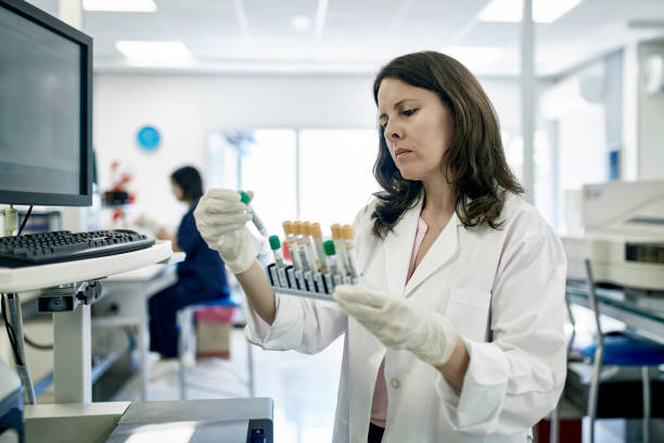 Mature Female Pathologist Examining Test Tube Samples in Lab Close-up of serious Hispanic female pathologist in white coat examining test tube rack samples in Buenos Aires clinical analysis laboratory. immunology stock pictures, royalty-free photos & images