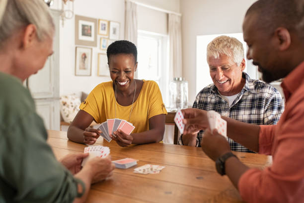 Mature friends playing cards at home Retired multiethnic people playing cards together at home. Happy senior friends with african couple playing cards. Cheerful active seniors playing game at lunch table. playing card stock pictures, royalty-free photos & images