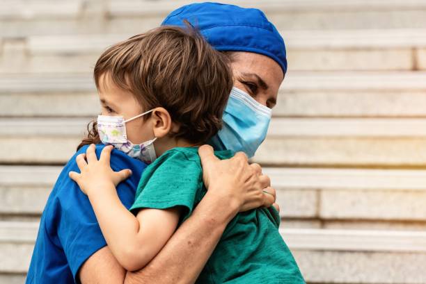 伝染性の大流行と戦うために病院から戻ってきた後、彼女の息子を抱きしめる成熟した医療従事者 - 退院 ストックフォトと画像