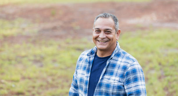 Mature Hispanic man wearing plaid shirt A mature Hispanic man in his 50s wearing a plaid shirt, standing in a park, looking at the camera, smiling. plaid shirt stock pictures, royalty-free photos & images