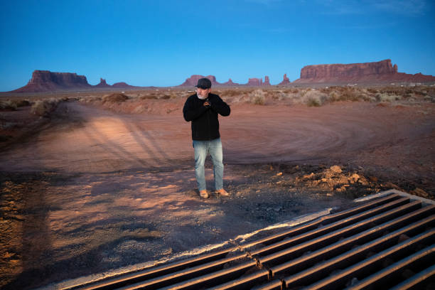 Mature Hispanic man wears a coat and keeps warm with gloves at night in front of vehicle headlights at the majestic buttes in the Monument Valley Tribal Park in Northern Arizona Navajo Country just after Sunset  cattle grid stock pictures, royalty-free photos & images